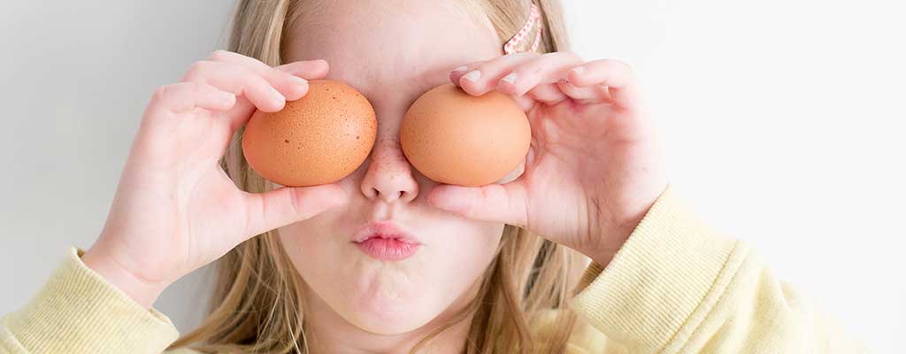 Ett barn håller två ägg framför sitt ansikte